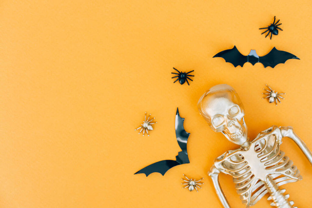 Scary and funny Halloween composition with spiders, bats and golden skeleton over orange background with copy space. Halloween party invitation template - Фото, изображение