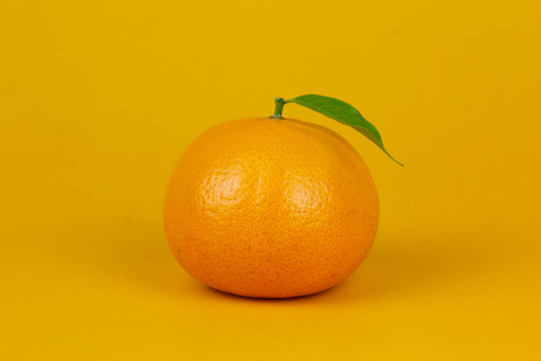 An Orange fruit with green leaf isolated on yellow background. One orange fruit with leaf stand on isolating concept for ads design - Φωτογραφία, εικόνα