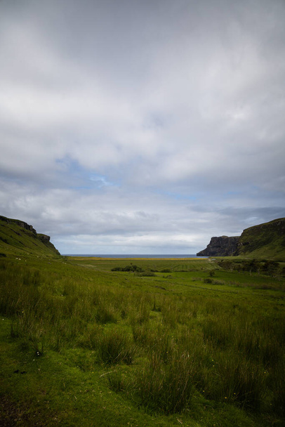 Wide angle views of Talisker Bay, Isle of Skye, Scotland, with its rocky beach, black stones, green fields, and a waterfall at the end of beach. Scattered clouds on blue sky, summer scottish weather. - Photo, Image