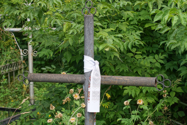 one black metal cross with a white funeral scarf on a grave in green vegetation in a cemetery - Valokuva, kuva