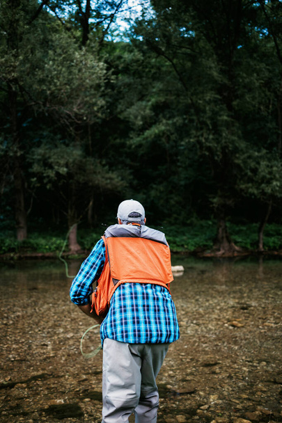 Senior man is fishing alone on fast mountain river. Active people and sport fly fishing concept. - Foto, Imagem