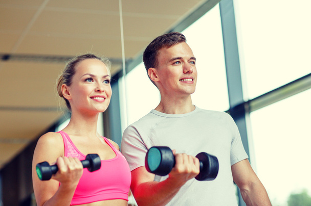 smiling young woman with personal trainer in gym - Foto, imagen