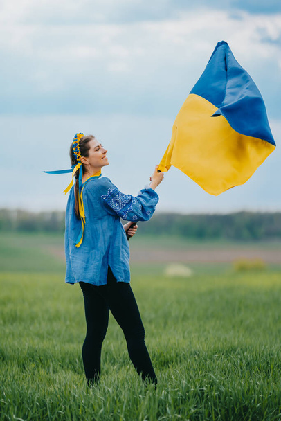Beautiful ukrainian woman with national flag on green field background. Young lady in blue embroidery vyshyvanka. Ukraine, independence, freedom, patriot symbol, victory in war. High quality photo - Fotó, kép