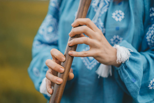 Woman playing woodwind wooden flute - ukrainian sopilka outdoors. Folk music, culture concept. Musical instrument. Lady in traditional embroidered shirt - blue vyshyvanka. High quality photo - Foto, Bild