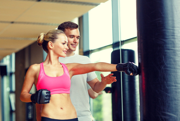 smiling woman with personal trainer boxing in gym - Foto, Bild