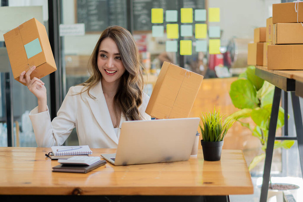 Beautiful Asian businesswoman working from home to shop online. Verify orders and prepare product packages with office equipment. Entrepreneurship and sme business lifestyle concept - 写真・画像