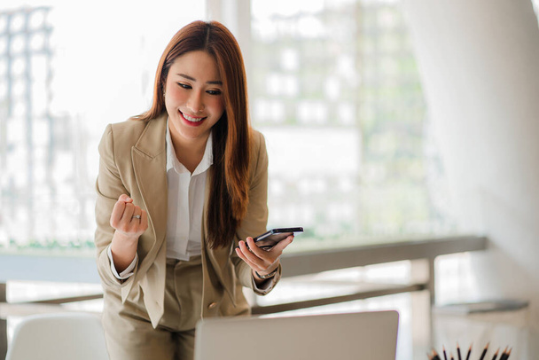 An Asian businesswoman uses a mobile phone while checking email or social media on the Internet. accounting finance concept and calculate with a calculator modern finance and accounting concepts - 写真・画像