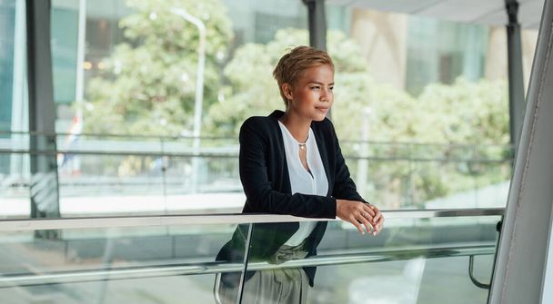 Successful businesswoman leaning on glass railing on a modern balcony - Photo, image