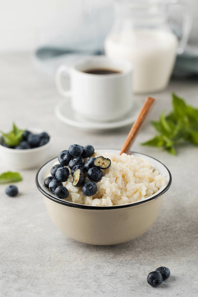 Rice pudding with blueberries in a bowl with a mug of coffee and a jug of milk on the table. Healthy gluten free breakfast recipe. - Valokuva, kuva