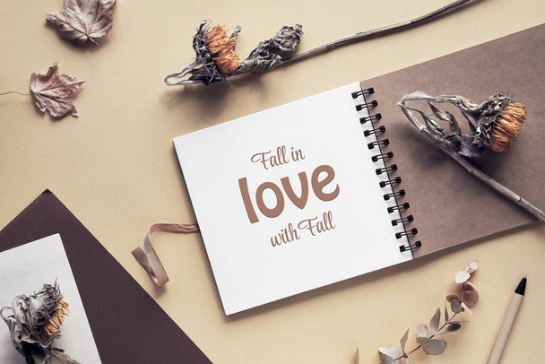 Caption motivator text Fall in love with Fall in square album, notebook with spiral binder. Wooden pen, dry sunflower flowers and maple leaves. Soft natural light. Monochromatic beige color hues. - Fotografie, Obrázek
