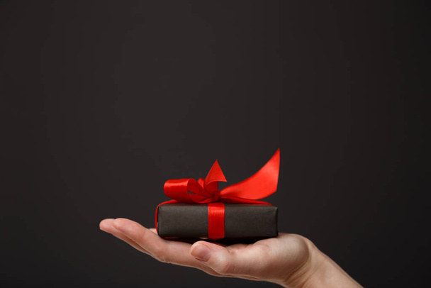 Woman's hand holding black gift box with red bow over black background. Black friday sale, Christmas sale, discount concept. Valentine's day. Father's day - Photo, image