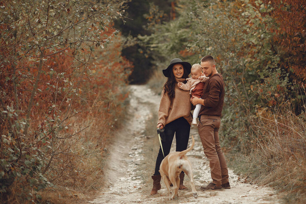 Family with cute little daughter. Father in a brown sweater. Family in a autumn field with dog - Foto, imagen