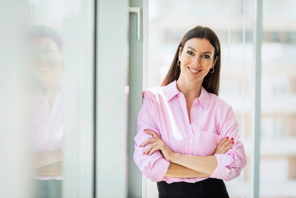 Portrait shot of an attractive businesswoman looking at camera and smiling while standing with arms crossed at the office. - 写真・画像