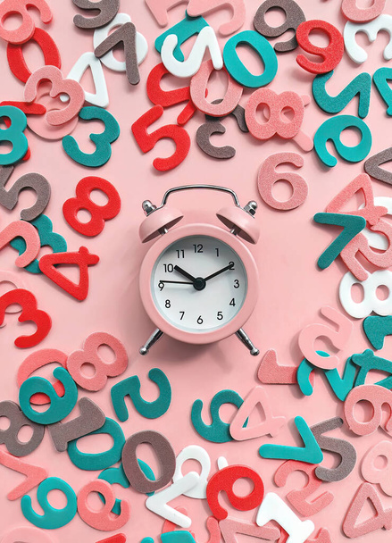 Pink alarm clock on pink background with colorful numbers flat lay. Back to school concept - Fotoğraf, Görsel