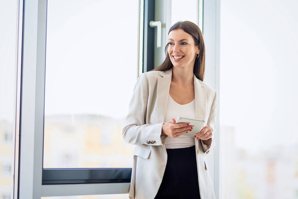Portrait of attractive businesswoman using digital tablet while standing at window in a modern office. - Fotoğraf, Görsel