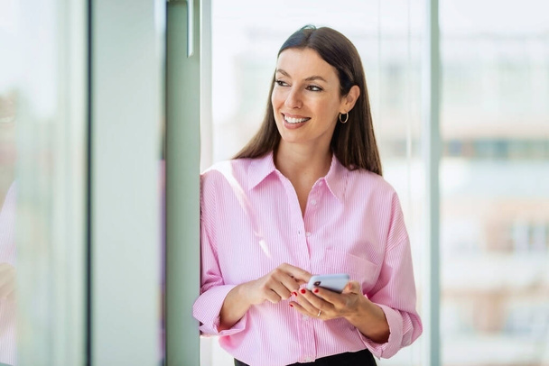 Attractive businesswoman looking thoughtfully while text messaging at the office. - 写真・画像