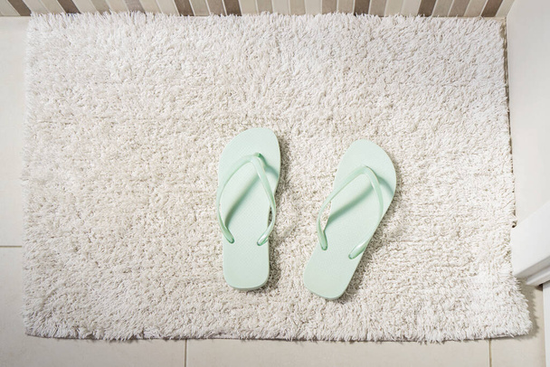 Pair peppermint-coloured flip-flops on white carpet in bathroom. Concept of cleanliness and personal care, top view - Foto, imagen
