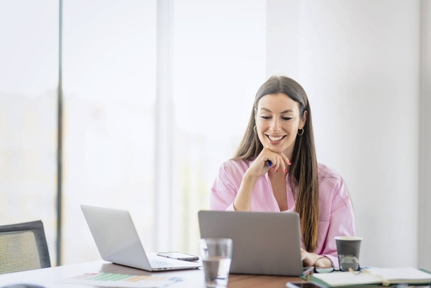 Smiling businesswoman using laptops while sitting at desk and working at a modern office. - Photo, image