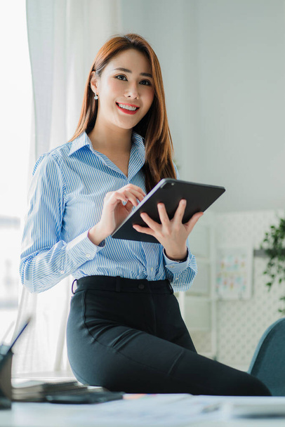Asian professional businesswoman holding a tablet standing by a glass plate window in the office - Foto, Imagen