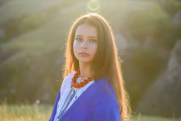 A teenage girl on the slope of a ravine with a Ukrainian flag on her shoulders. - Fotografie, Obrázek