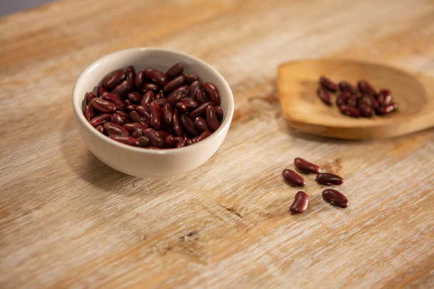 Red kidney beans in a spoon and in a bowl on wooden background - Фото, изображение