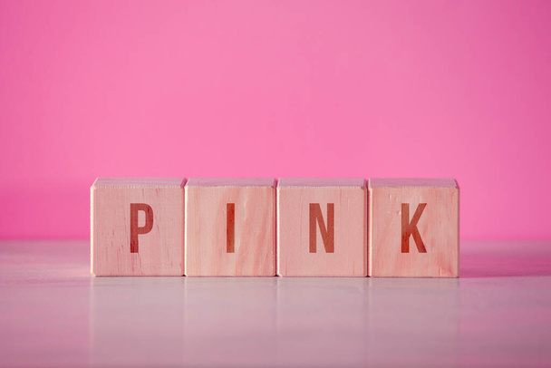 Four wooden cubes with the written word "pink" on pink background - Fotó, kép