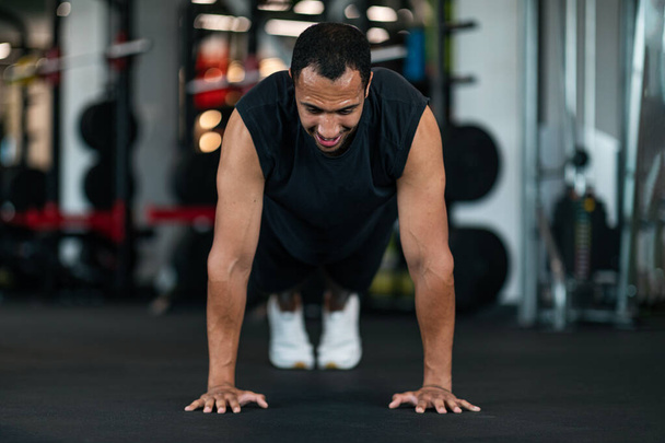 Athletic Black Man Making Floor Push Up Exercise While Training In Gym, Muscular African American Male Exercising In Modern Sport Club, Practicing Bodybuilding, Front View With Copy Space - Photo, image
