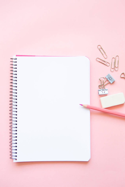 pink pencil and stationery items on notepad with blank page and on pink background - Photo, image