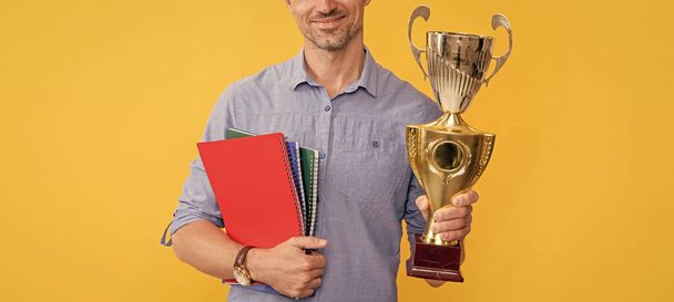 hymyilevä mies pitää mestari cup ja muistikirja keltaisella pohjalla, palkinto. - Valokuva, kuva