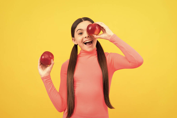happy kid with red apple on yellow background, vitamins. - Foto, immagini