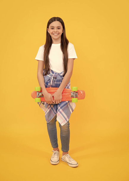 Happy girl child in casual holding skateboard yellow background, pennyboard. - Photo, image