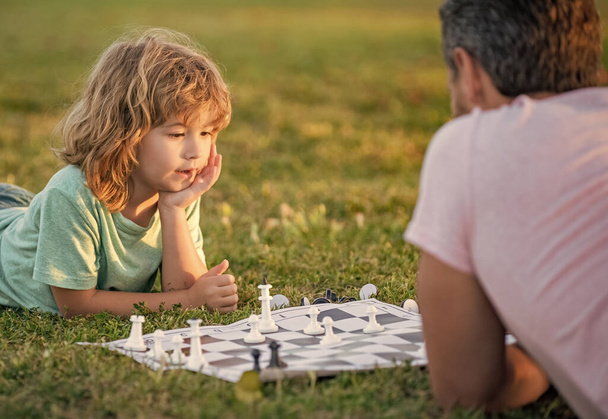 onnellinen perhe mies vanhempi ja poika poika pelaa shakkia vihreällä ruoholla puistossa ulkona, lapsuuden kehitys. - Valokuva, kuva