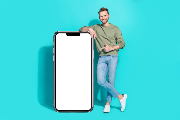 Photo of confident man direct finger white card empty space wear pullover jeans isolated blue color background. - Foto, Bild