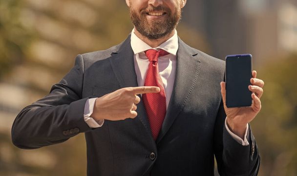 brodaty biznesmen w formalnym ubraniu wskazujący palcem na telefon przed biurem, cyber poniedziałek. - Zdjęcie, obraz