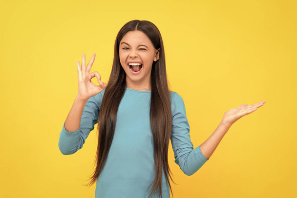 boldog tini lány ok gesztus bemutató termék sárga háttér másolási hely, reklám. - Fotó, kép