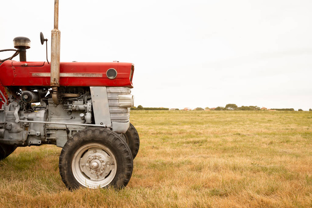 Detail of the front of a tractor standing in a crop field. The day is cloudy. Concept of agriculture and rural life. Space for text. - 写真・画像