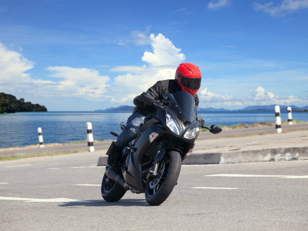 молодий чоловік їде на великому мотоциклі проти гострої кривої асфи
 - Фото, зображення