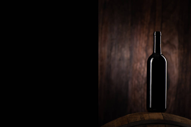 A Red wine bottle on wodden barrel with a wooden backgorund close up - Foto, imagen