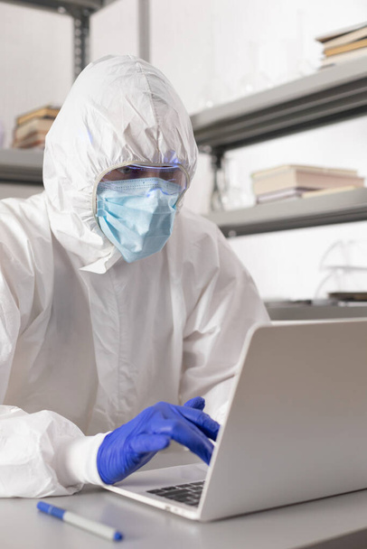 Vědec pracující na notebooku se dívá na zkumavku s kapalným činidlem. Laboratorní vědec a chemické laboratorní sklo - Fotografie, Obrázek