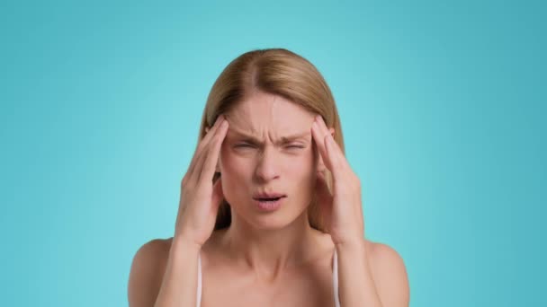 Migraine concept. Close up portrait of middle aged woman suffering from acute headache, massaging her painful temples, blue studio background, slow motion - Metraje, vídeo