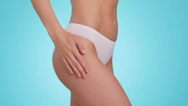 Body care concept. Close up shot of unrecognizable woman applying anti cellulite or anti stretch marks cream on her hips, blue studio background, slow motion - Filmagem, Vídeo