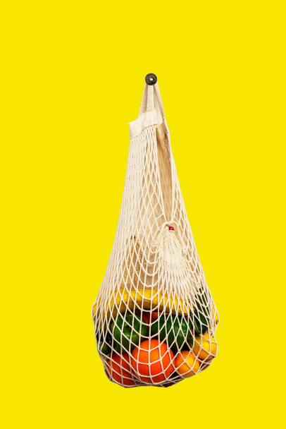 White string bag with different vegetables and fruits on a yellow background. top view - Фото, зображення