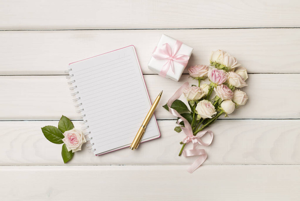 Notebook, gift box and rose flowers on wooden background, top view. - Fotó, kép