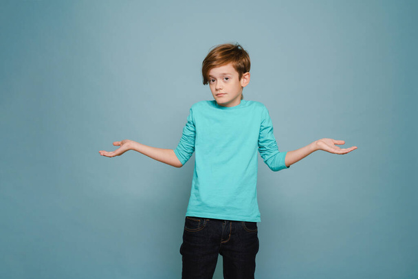 Ginger perplexed boy gesturing and looking at camera isolated over blue wall - Фото, зображення