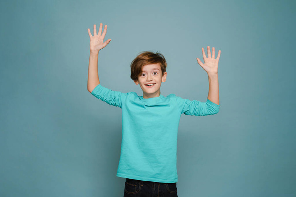 Ginger white boy wearing long sleeve smiling and gesturing at camera isolated over blue wall - Zdjęcie, obraz