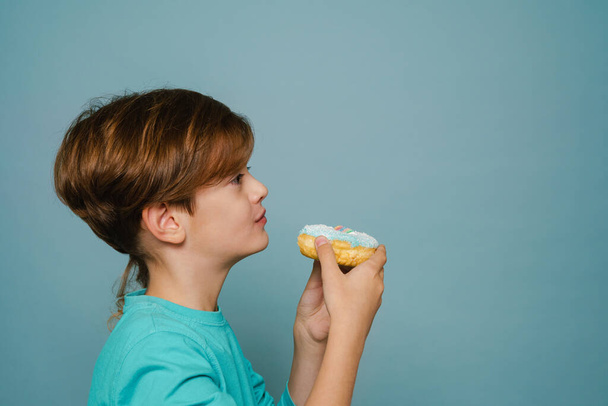 Ginger white boy wearing long sleeve eating doughnut isolated over blue wall - Foto, immagini