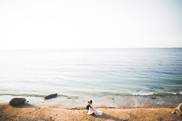 Wedding couple kissing and hugging on rocks near blue sea. - Фото, зображення