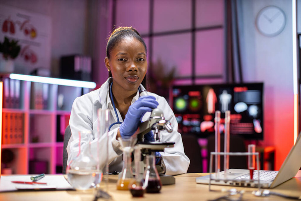 Modern medical research laboratory: portrait of african scientist working, using microscope, analyzing samples. Advanced scientific pharmaceutical lab for medicine, biotechnology development. - Photo, image