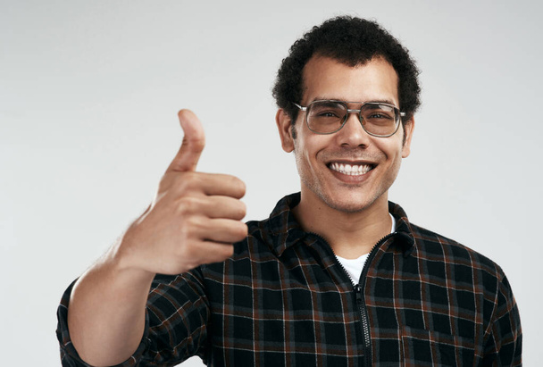 Im onboard. a handsome young man showing thumbs up while standing against a grey background - Fotó, kép