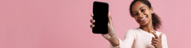 Black girl pointing finger and showing cellphone at camera isolated over pink background - Foto, Bild